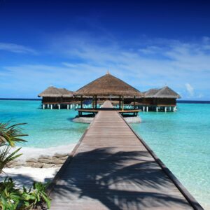 Scenic view of a wooden boardwalk leading to serene overwater bungalows at an island resort.